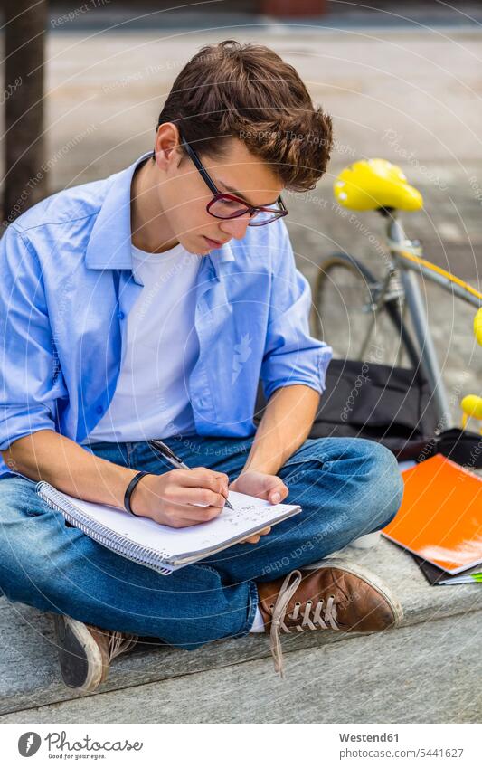 Young man with racing cycle sitting on bench writing on notepad student students learning write education University Student University Students benches Seated