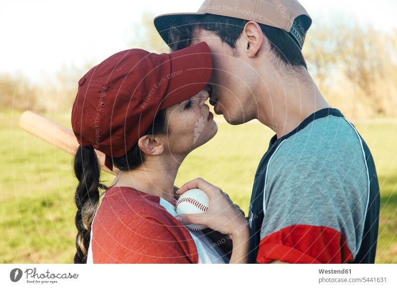 Young couple with baseball equipment kissing in park baseball player baseball players twosomes partnership couples kisses sport sports people persons