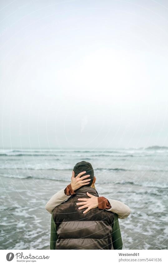 Woman embracing man at the seafront in winter couple twosomes partnership couples embrace Embracement hug hugging Sea ocean people persons human being humans