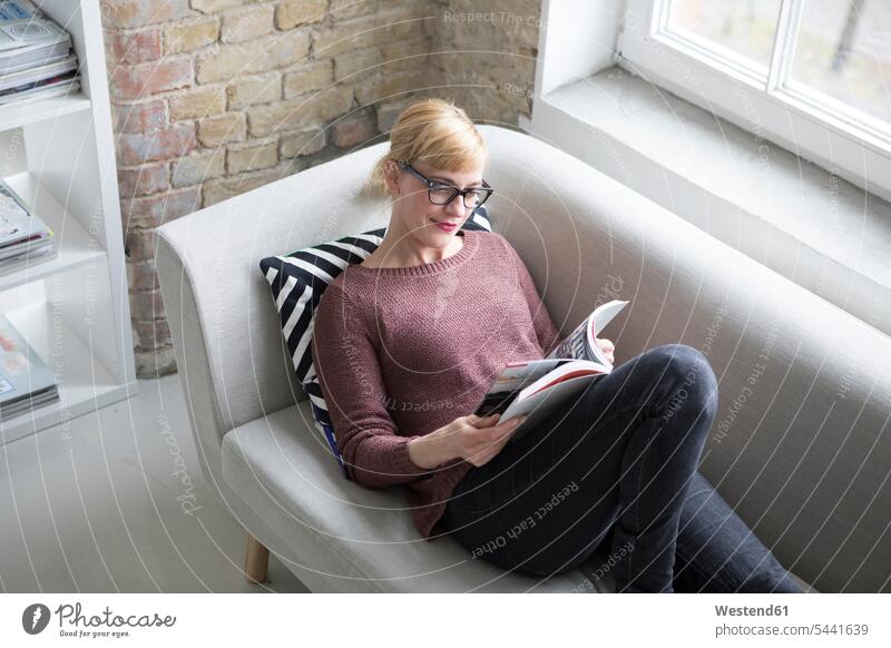 Woman sitting on couch, reading book woman females women relaxation relaxed relaxing books home at home settee sofa sofas couches settees resting Adults