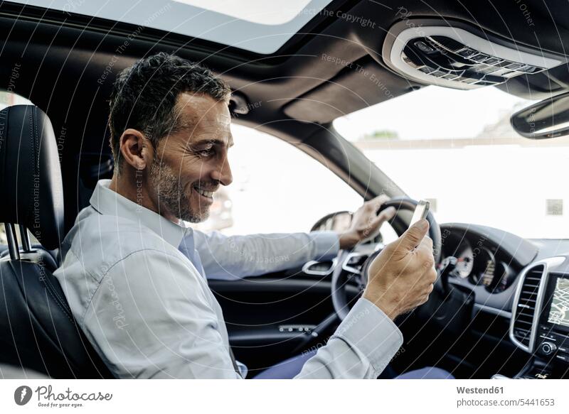 Businessman driving car looking at cell phone drive Business man Businessmen Business men mobile phone mobiles mobile phones Cellphone cell phones smiling smile