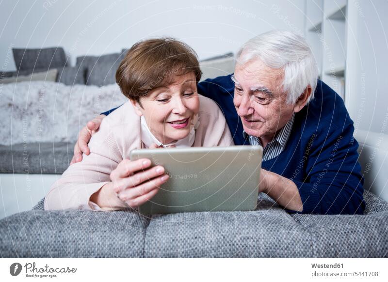 Senior couple lying on couch using digital tablet settee sofa sofas couches settees digitizer Tablet Computer Tablet PC Tablet Computers iPad Digital Tablet