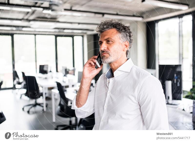 Mature businessman on cell phone in office offices office room office rooms Businessman Business man Businessmen Business men mobile phone mobiles mobile phones