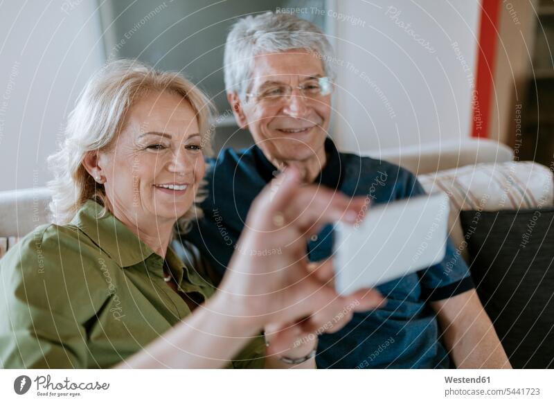 Senior couple at home sitting on couch taking a selfie Selfie Selfies mobile phone mobiles mobile phones Cellphone cell phone cell phones twosomes partnership
