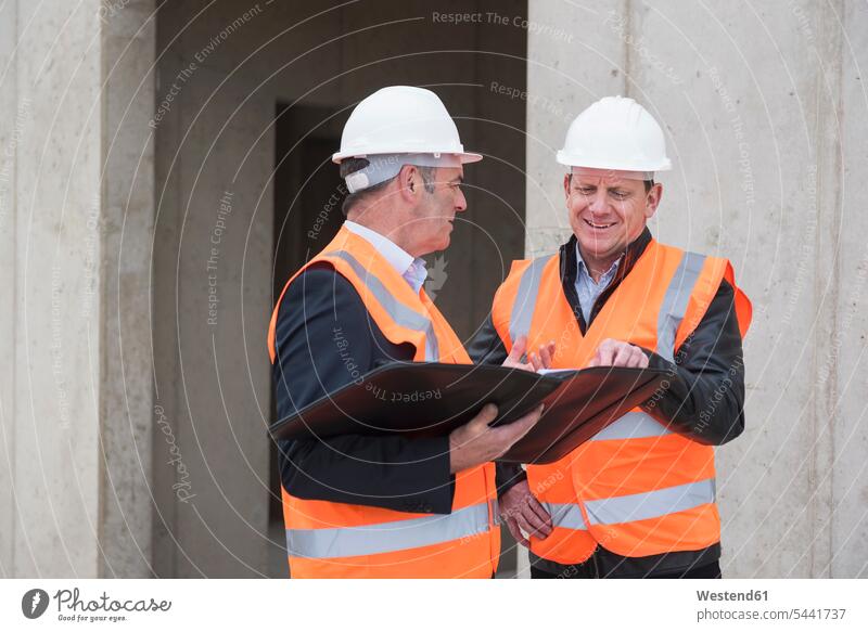 Two men wearing safety vests talking on construction site working At Work speaking man males architect architects Building Site sites Building Sites