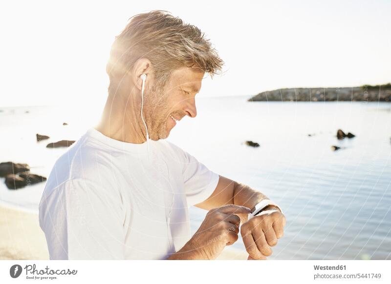 Mature man with earphone checking his smartwatch after yogging on the beach men males smart watch Adults grown-ups grownups adult people persons human being