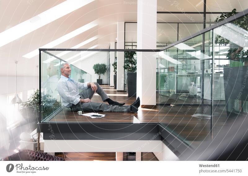 Businessman sitting on floor in the office, taking a break Taking a Break resting Business man Businessmen Business men smiling smile Seated offices office room