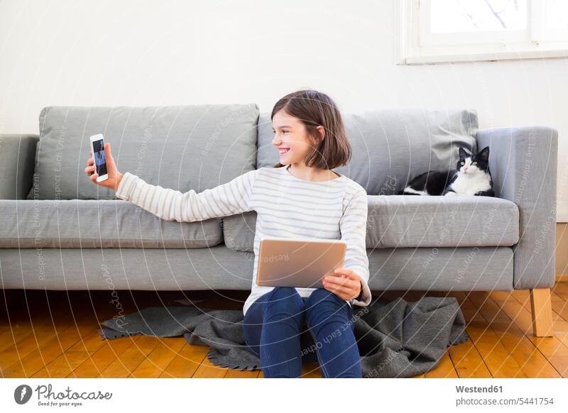 Happy girl with tablet sitting on the floor of the living room taking selfie with smartphone Seated Selfie Selfies Floor Floors living rooms livingroom