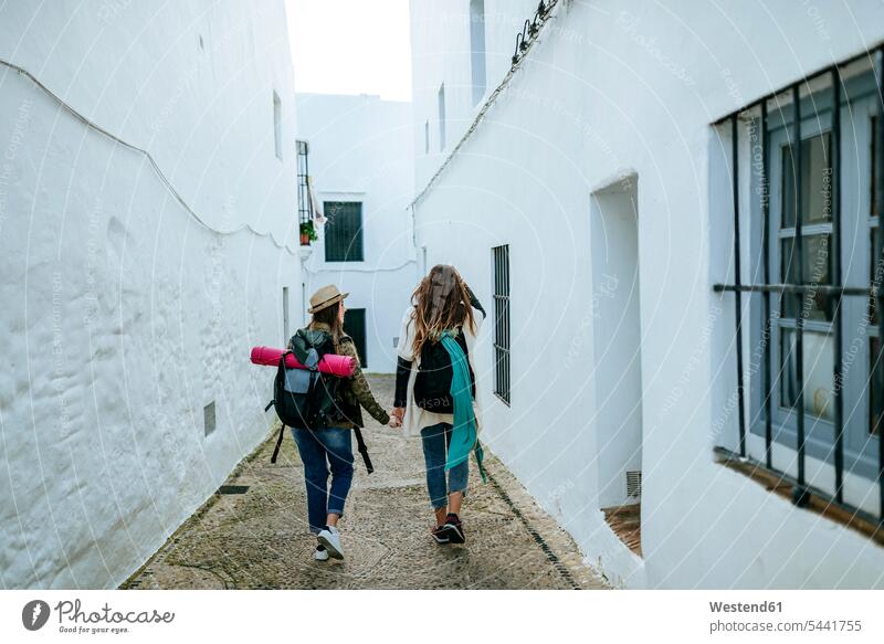 Two young women on a trip walking in a town holding hands female friends going mate friendship female tourist city cities towns woman females tourists tourism
