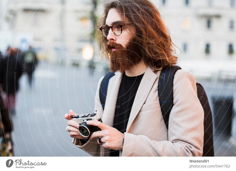 Stylish young man outdoors holding camera looking around photographer photographers men males cameras Adults grown-ups grownups adult people persons human being