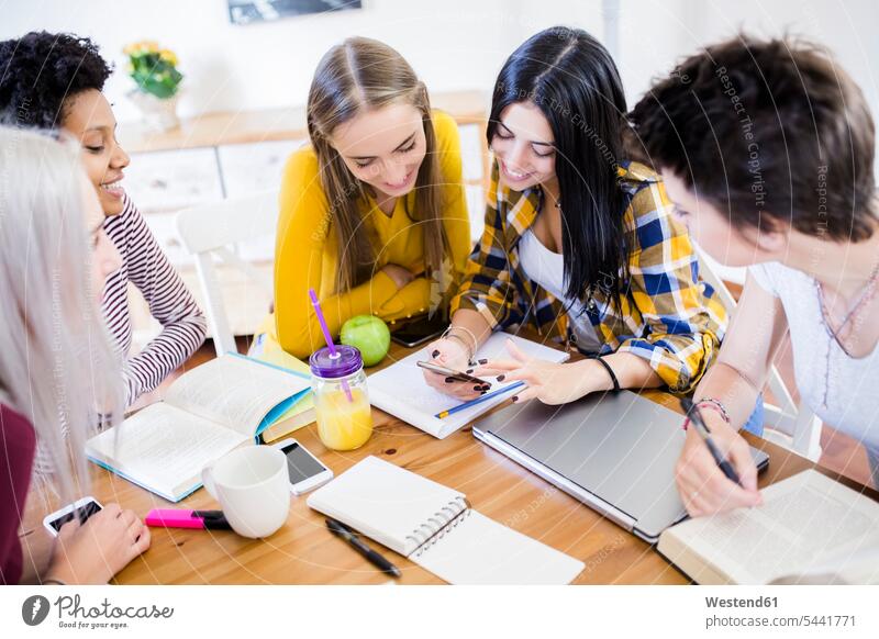 Group of female students sharing cell phone at table at home share Table Tables woman females women mobile phone mobiles mobile phones Cellphone cell phones