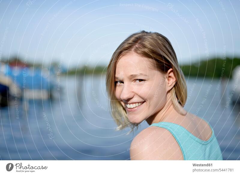 Portrait of smiling young woman in front of a lake portrait portraits smile females women Adults grown-ups grownups adult people persons human being humans