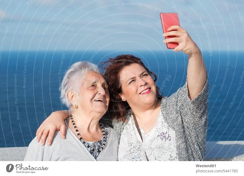 Grandmother and granddaughter taking a selfie in front of the sea granddaughters grandmother grandmas grandmothers granny grannies portrait portraits grandchild