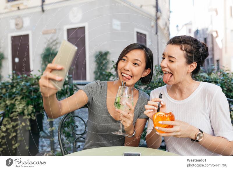 Italy, Padua, two young women pulling funny faces while taking selfie at sidewalk cafe female friends Selfie Selfies mate friendship Smartphone iPhone