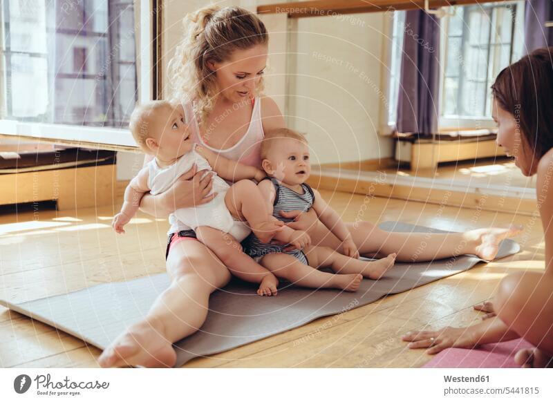 Mother with twin babies sitting on yoga mat mother mommy mothers mummy mama smiling smile baby infants nurselings exercising exercise training practising Fun