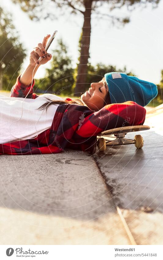 Young woman lying on skateboard looking at cell phone laying down lie lying down smiling smile Skate Board skateboards mobile phone mobiles mobile phones