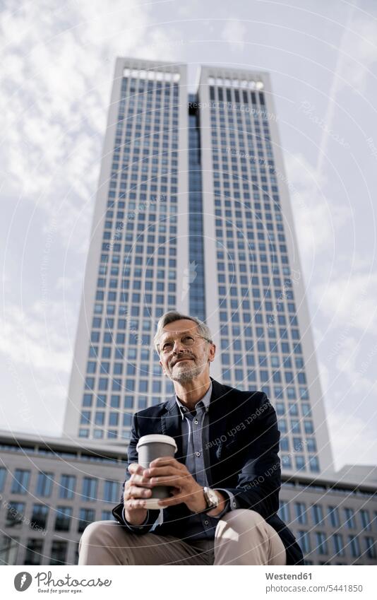 Grey-haired businessman in front of skyscraper holding coffee to go sitting Seated Coffee Businessman Business man Businessmen Business men skyscrapers