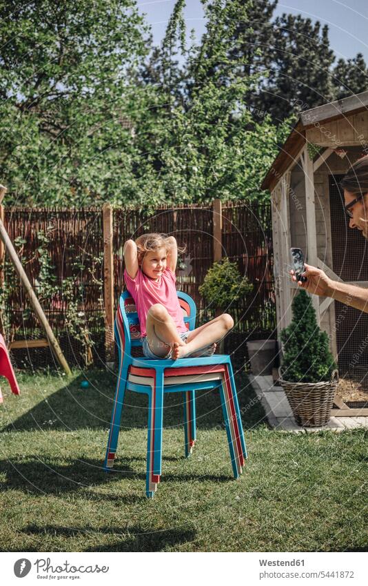 Father taking cell phone picture of daughter sitting on chair in garden daughters mobile phone mobiles mobile phones Cellphone cell phones gardens