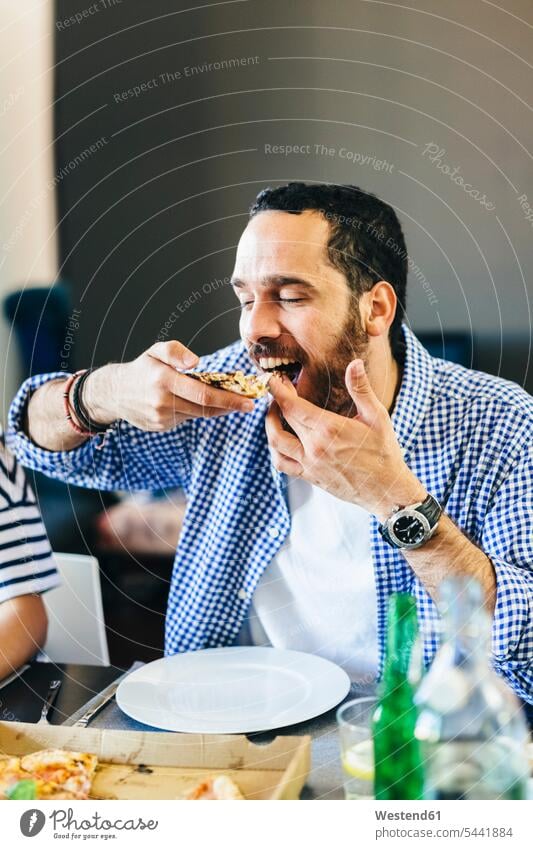 Young man enjoying slice of pizza at dining table men males Pizza Pizzas eating Adults grown-ups grownups adult people persons human being humans human beings