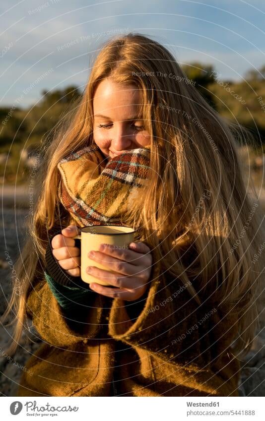 Smiling young woman holding hot drink in nature smiling smile mug mugs cup females women Adults grown-ups grownups adult people persons human being humans