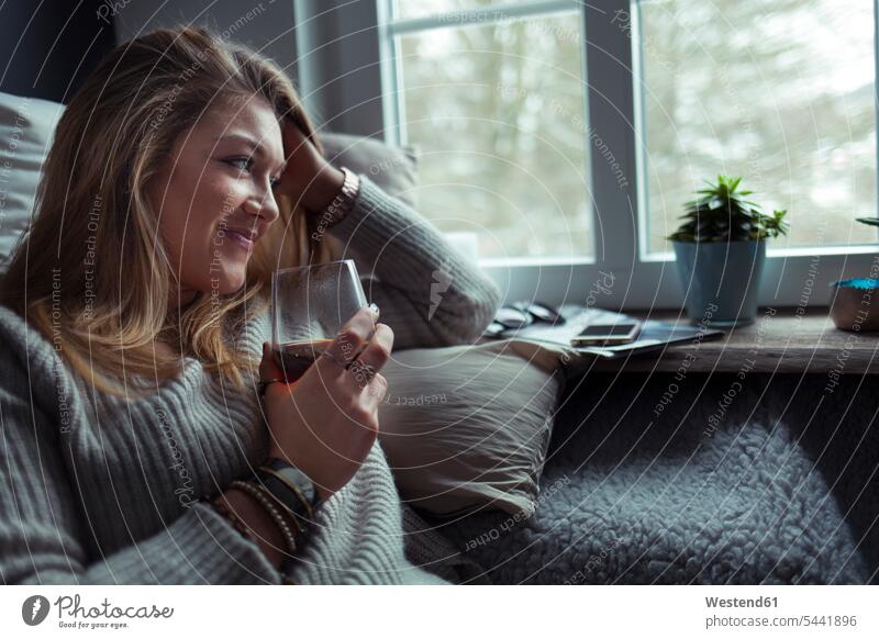 Smiling blond woman with glass of coffee relaxing on couch at home females women settee sofa sofas couches settees Adults grown-ups grownups adult people