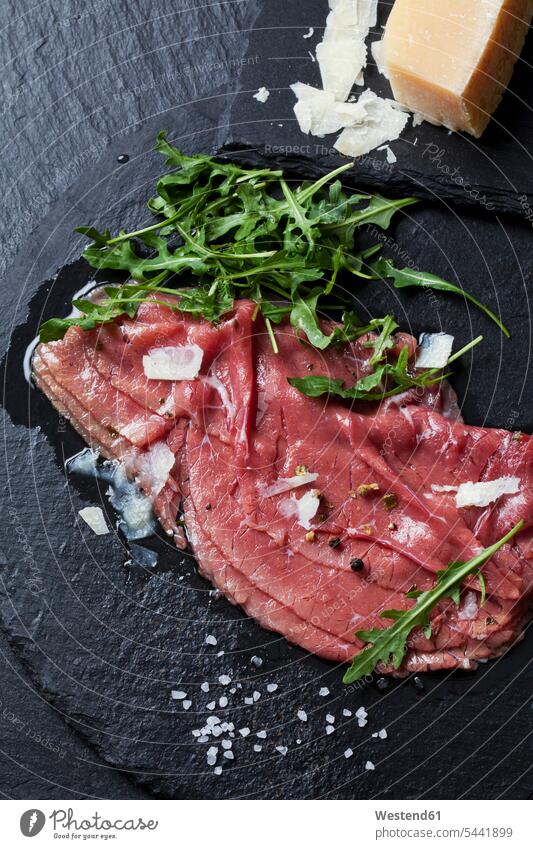 Beef Carpaccio with rocket, olive oil, parmesan, pepper and salt on slate nobody Salt Table Salt Cooking Salt topping garnished Toppings Topped Pepper