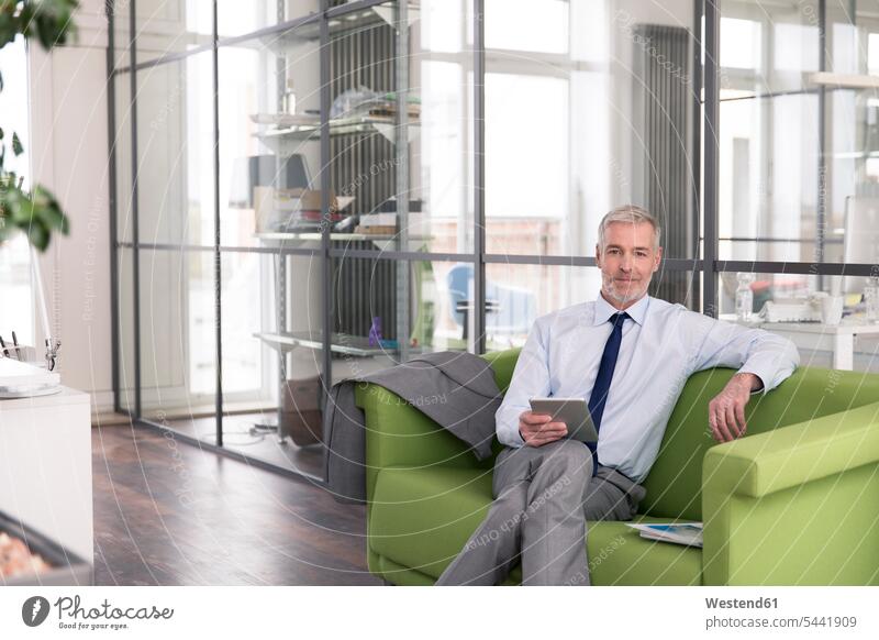 Mature businessman sitting on a couch in the office, holding digital tablet caucasian caucasian ethnicity caucasian appearance european confidence confident