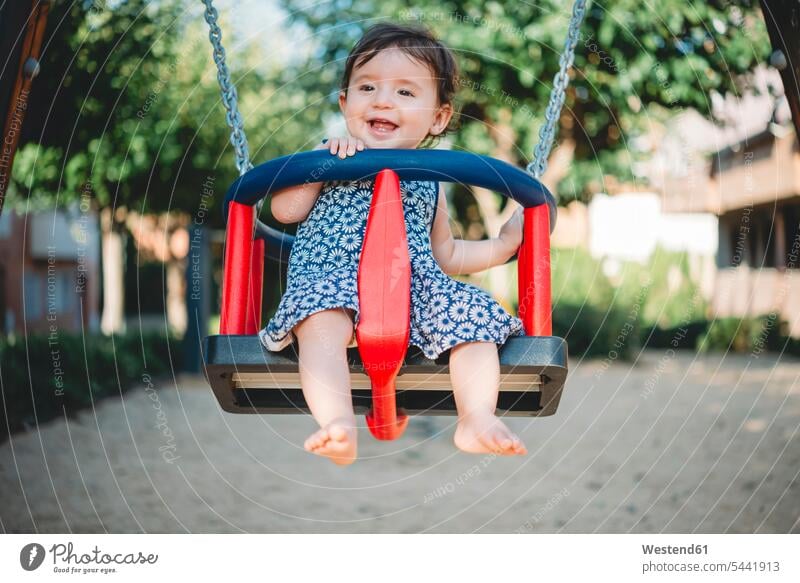 Portrait of laughing baby girl sitting in swing on playground swing set swingset baby girls female portrait portraits babies infants people persons human being