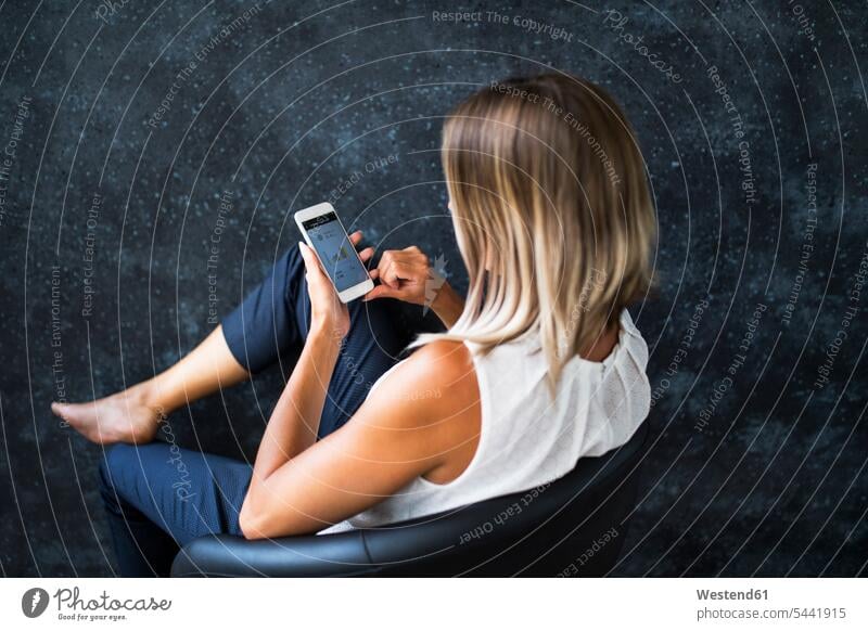 Businesswoman sitting in armchair checking data on cell phone Seated businesswoman businesswomen business woman business women females mobile phone mobiles
