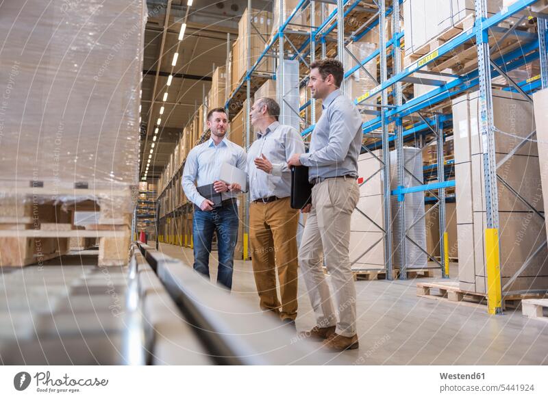 Three men talking in factory warehouse colleagues storehouse storage working At Work speaking man males dumps stock Adults grown-ups grownups adult people