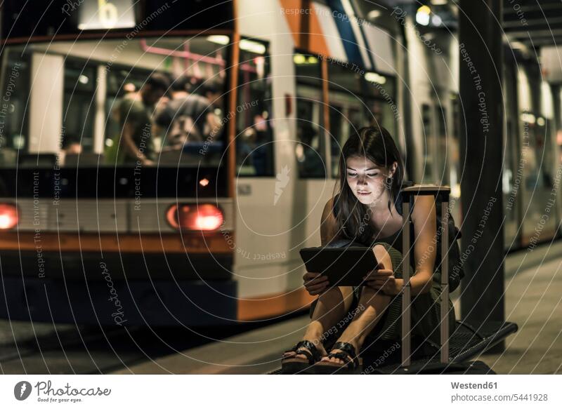 Portrait of young woman waiting at tram stop by night using tablet at night nite night photography females women Adults grown-ups grownups adult people persons