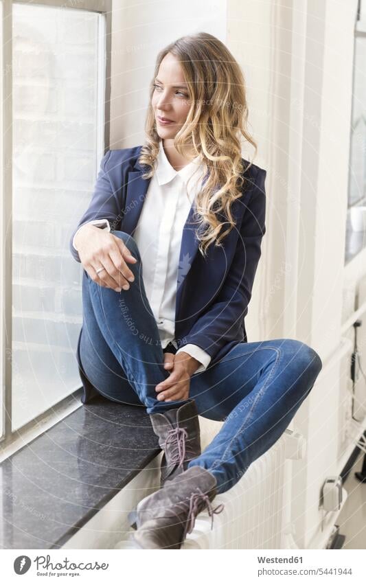 Businesswoman sitting on window sill of her office offices office room office rooms businesswoman businesswomen business woman business women entrepreneur