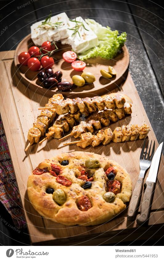 Meat skewers, flat bread, sheep cheese, tomatoes and olives on wooden board grilled barbecued ewe's cheese rosemary black olive black olives Cherry Tomato
