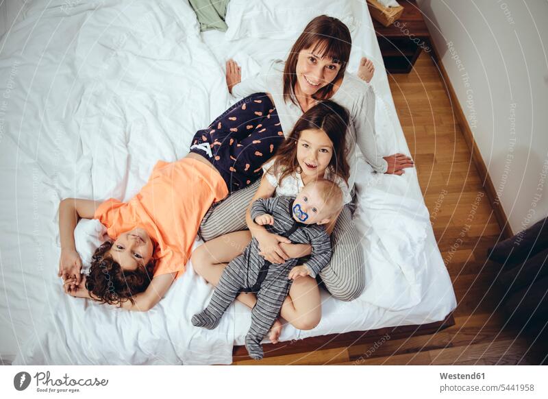 Happy mother in bed with her three children family families portrait portraits mommy mothers ma mummy mama smiling smile beds people persons human being humans