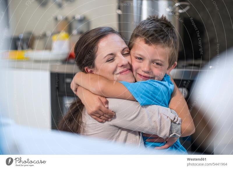 Mother and son hugging in kitchen domestic kitchen kitchens embracing embrace Embracement mother mommy mothers ma mummy mama sons manchild manchildren parents