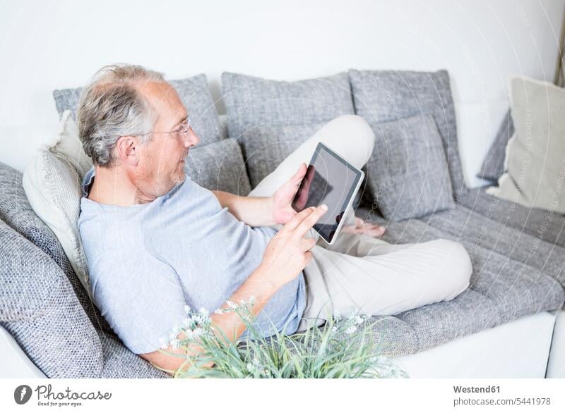 Mature man at home lying on couch using digital tablet men males settee sofa sofas couches settees relaxed relaxation digitizer Tablet Computer Tablet PC