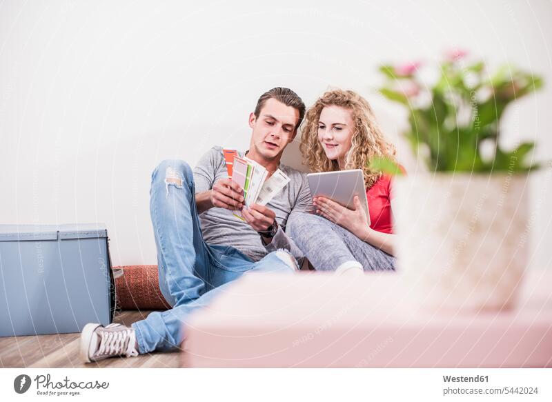 Young couple in new home sitting on floor with tablet choosing from color sample flat flats apartment apartments twosomes partnership couples select choose