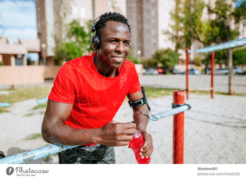 Portrait of relaxed young man with isotonic drink listening music with headphones men males portrait portraits Adults grown-ups grownups adult people persons