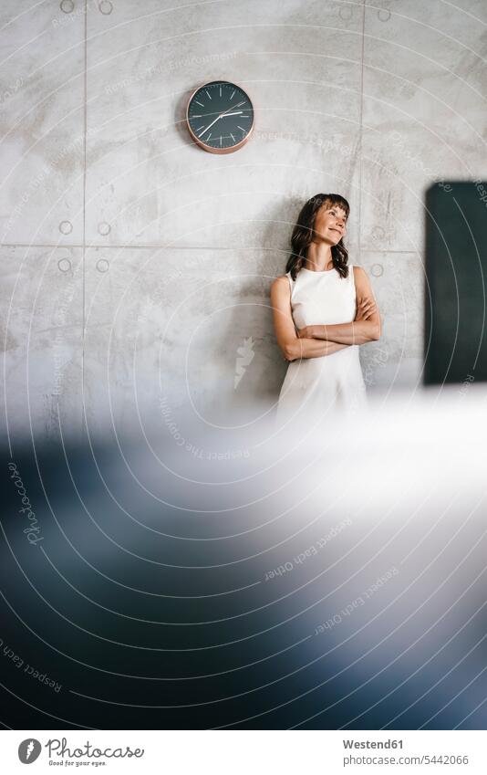 Businesswoman standing under wall clock with arms crossed businesswoman businesswomen business woman business women Clock Clocks females daydreaming
