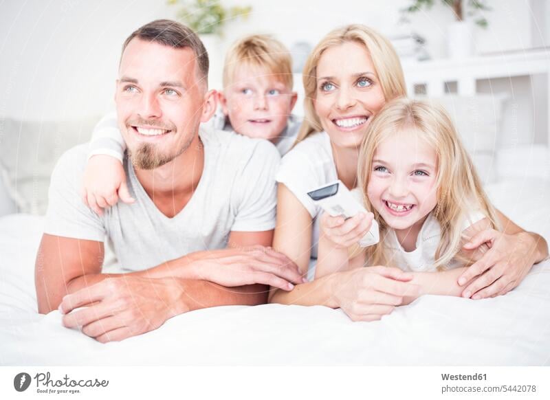Happy family lying in bed watching Tv beds families smiling smile relaxed relaxation portrait portraits watching TV Looking At Tv watching television