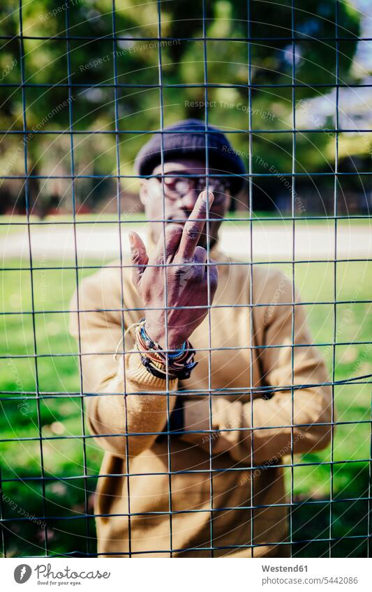Man behind a metal net giving the finger fingers man men males cool attitude composed coolness laid-back portrait portraits serious earnest Seriousness austere