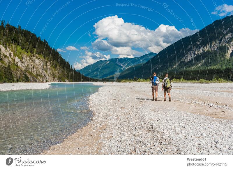 Germany, Bavaria, back view of two hikers with backpacks walking in dry creek bed trekking friends wanderers friendship hiking river bed riverbed going