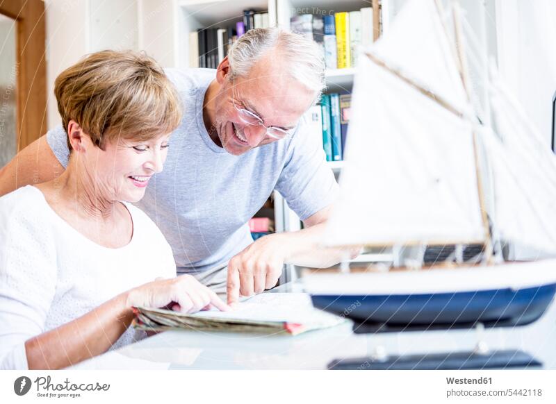 Senior couple at desk with magazine and model ship twosomes partnership couples smiling smile people persons human being humans human beings magazines