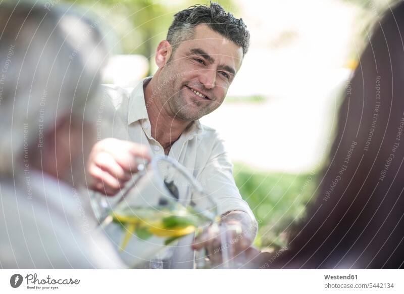 Smiling man pouring lemonade into glass in garden celebrating celebrate partying friends smiling smile group of people Group groups of people friendship persons