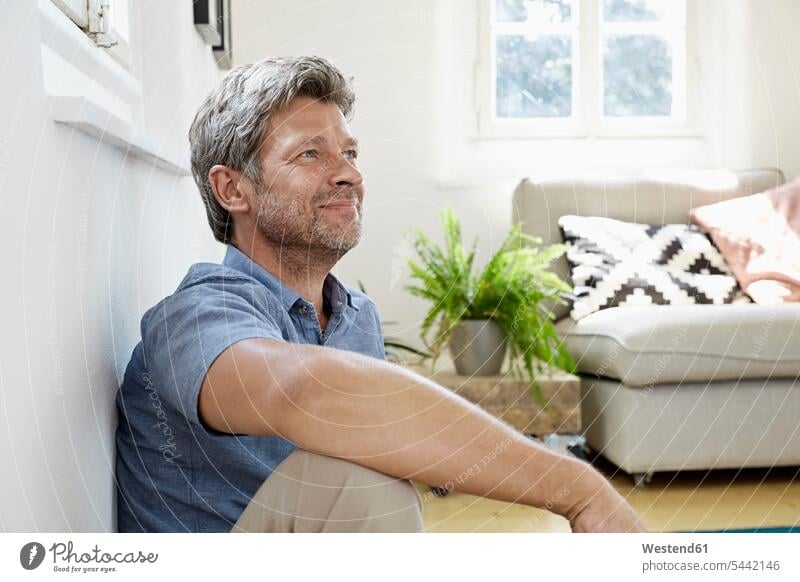 Mature man at home sitting in front of couch Seated sitting on ground Sitting On The Floor Sitting On Floor men males Adults grown-ups grownups adult people