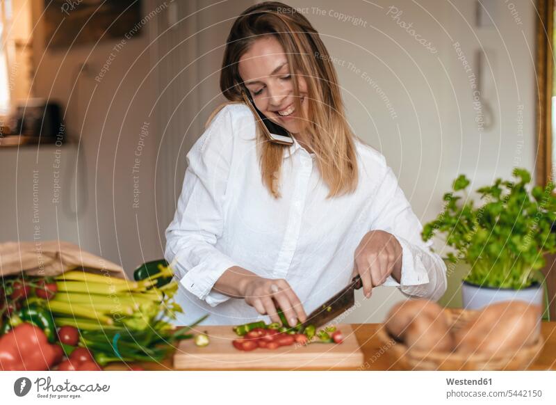 Smiling woman on the phone chopping vegetables in the kitchen call telephoning On The Telephone calling females women telephone call Phone Call using phone