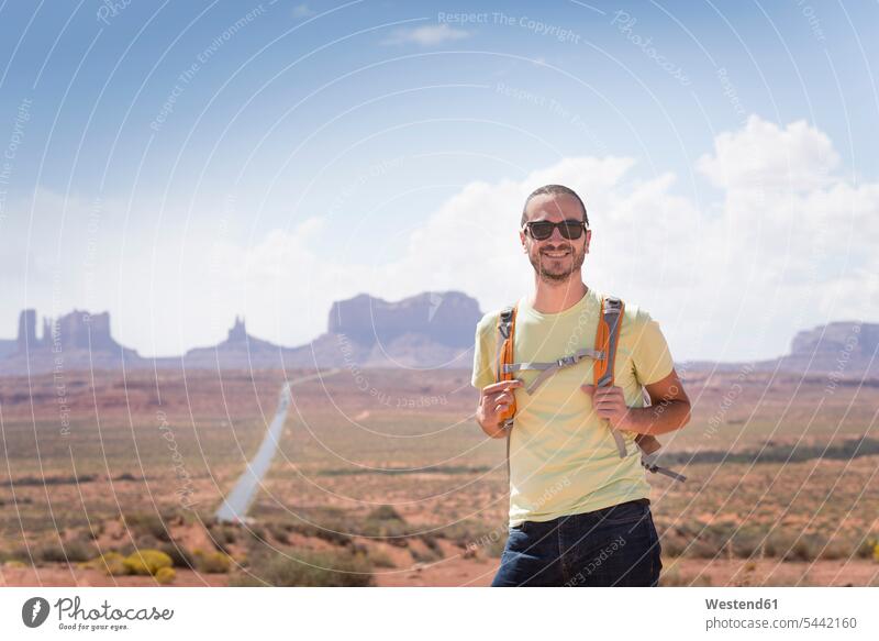 USA, Utah, portrait of smiling man with backpack and sunglasses on road to Monument Valley males portraits Adults grown-ups grownups adult people persons