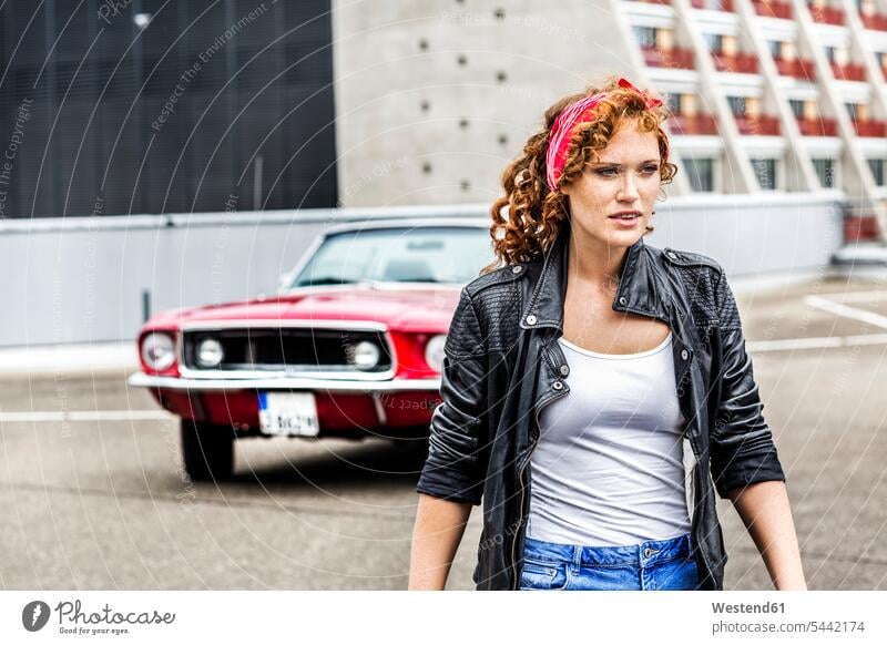 Redheaded woman next to sports car on parking level females women automobile Auto cars motorcars Automobiles portrait portraits Adults grown-ups grownups adult