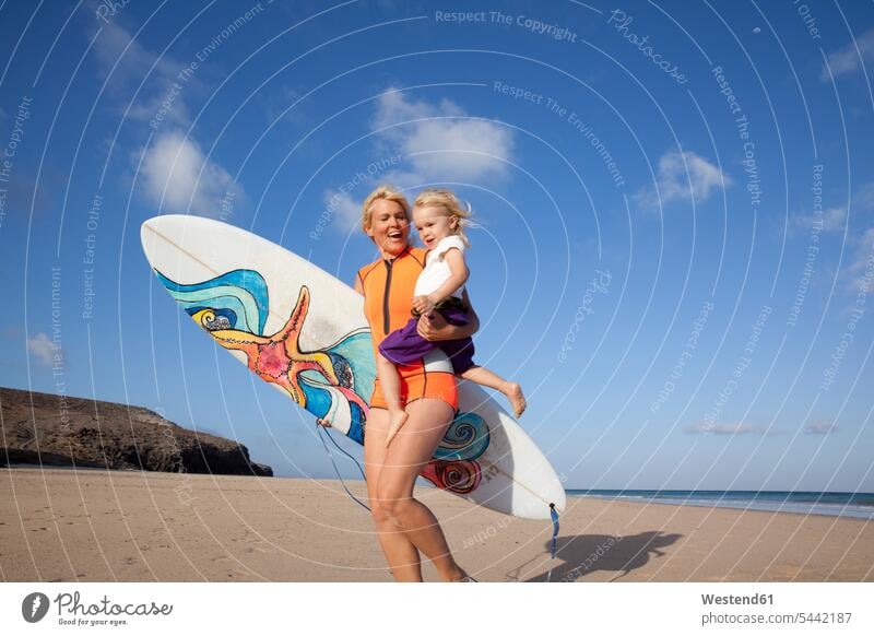 Spain, Fuerteventura, happy mother and daughter walking with surfboard on the beach Fun having fun funny mommy mothers ma mummy mama daughters surfboards going