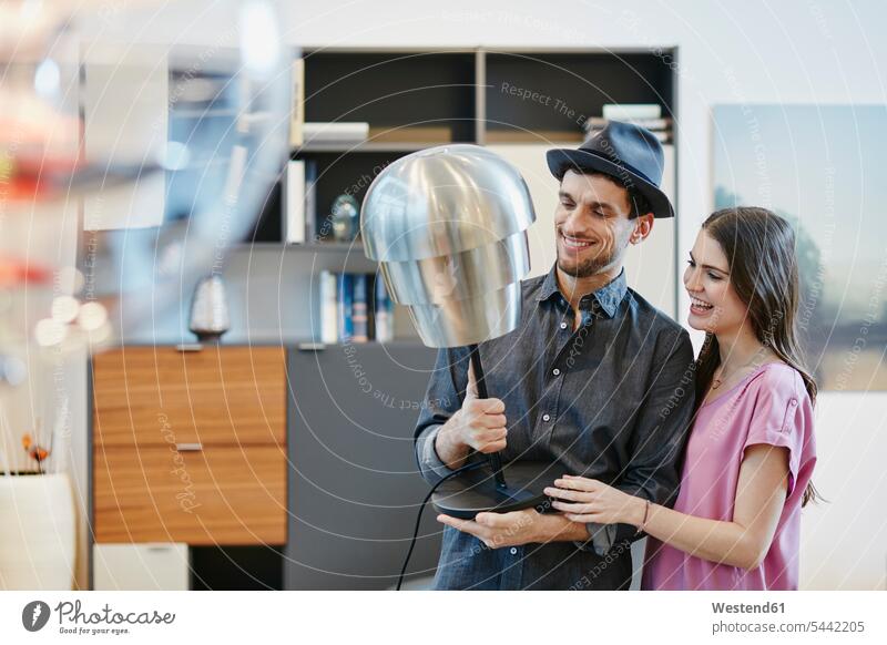 Couple in furniture store choosing lamp lamps laughing Laughter couple twosomes partnership couples select choose selecting lighting illumination positive